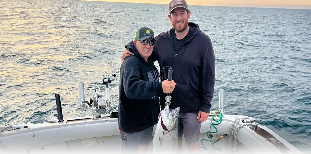 Two anglers pose at dusk on the stern with a salmon on a gaff